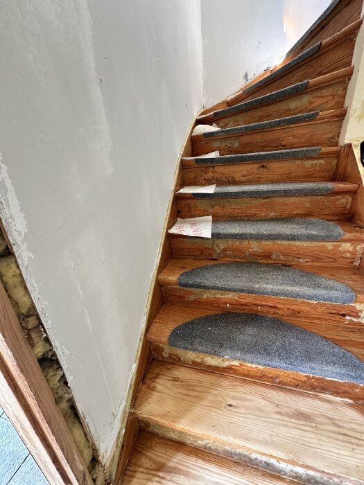 Trätrappa med gråa halkskydd och sliten yta, vägg i behov av renovering, del av ett bygge eller renoveringsprojekt.