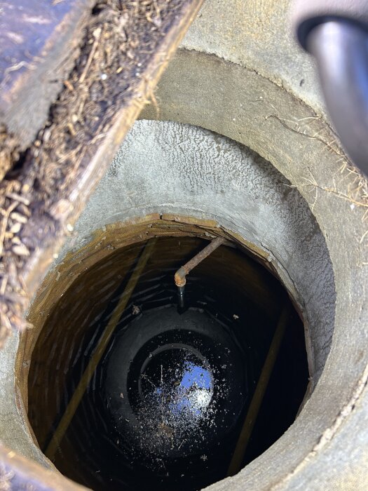 Öppen brunn med synligt rör och vattenyta i botten, sedd ovanifrån.