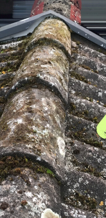 Taknock med felmonterad och skadad plåt, täckt med mossa och påväxt. Plåten är knäckt felaktigt över taknocken.