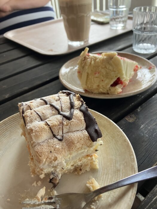 Kakor på tallrikar placerade på ett svart bord, en med chokladglasyr och en med vit choklad och bär. Bakom står ett glas med kaffe och vatten.