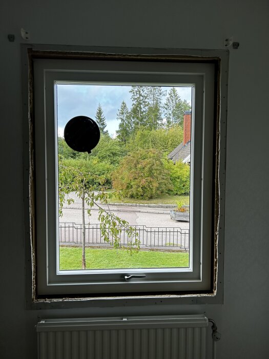 Nytt treglasfönster installerat med utsikt över grönskande trädgård och gata, gammal drevning synlig runt ramen.