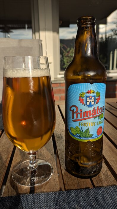 Glas och flaska av Primátor Oktoberlager på altanbord i solen.