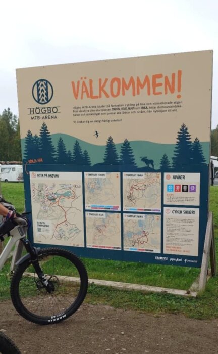 Informationsskylt vid Högbo MTB Arena med karta och cykelleder, delvis skymd av en cyklist.