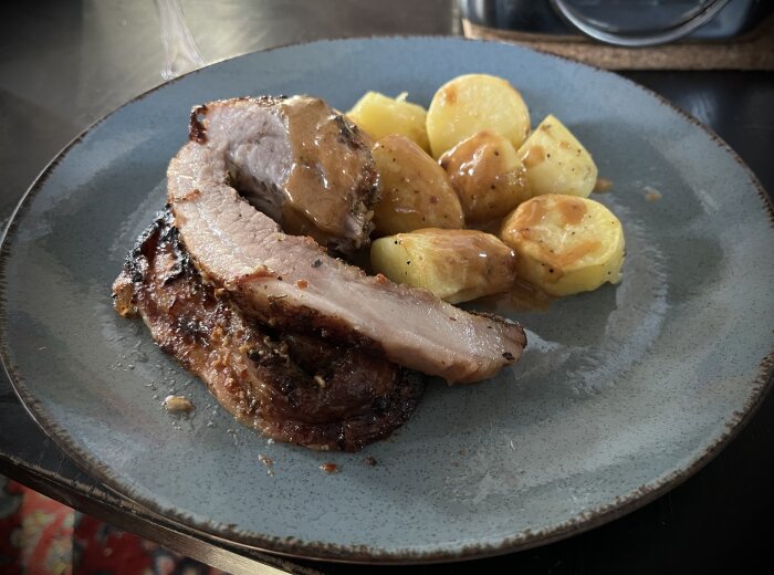 Porchetta med ugnsstekt potatis på tallrik.