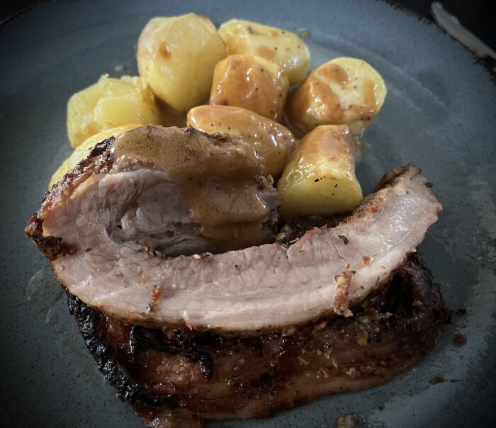 Porchettaskiva med ugnsstekta potatisklyftor på tallrik, serverad med sås.