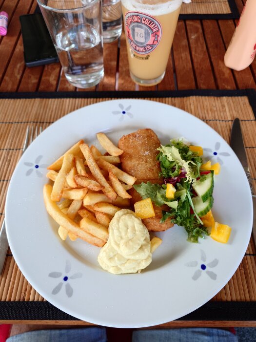 Tallrik med fisk och pommes frites, remouladsås samt sallad på ett bord med dryck i glas.