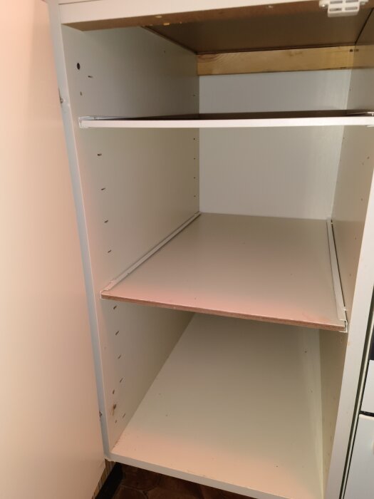 Tomt köksskåp utan dörrar och med hyllplan, fastsatt i väggen. Skåpet ska tas bort försiktigt för att inte skada det.