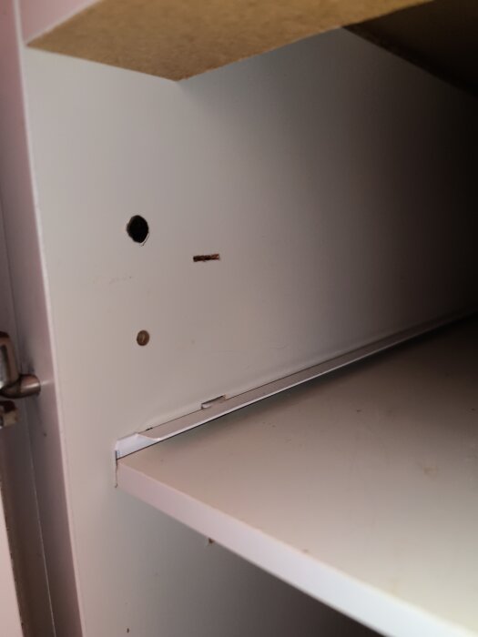 Interiör av köksskåp med spik i väggen och plastskruvar.