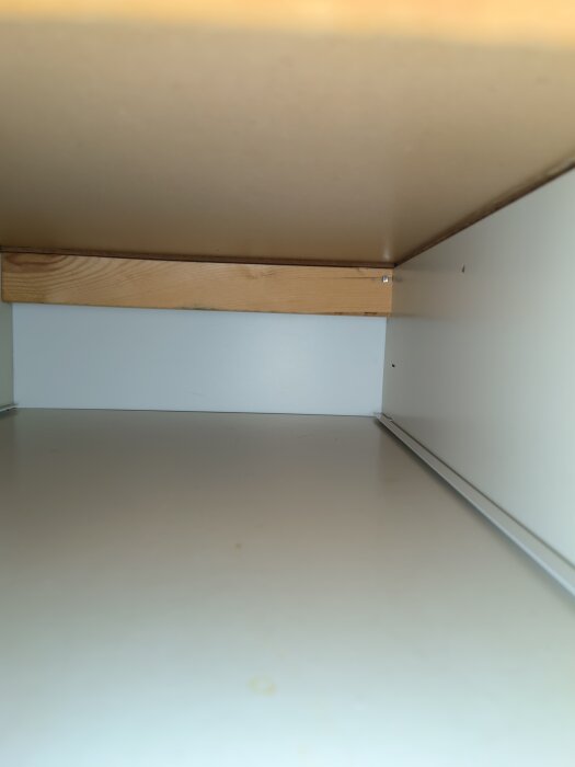 Inuti ett köksskåp med vit insida och träram fäst vid väggen. Skåpet sägs vara svårt att ta bort på grund av fästanordningarna.