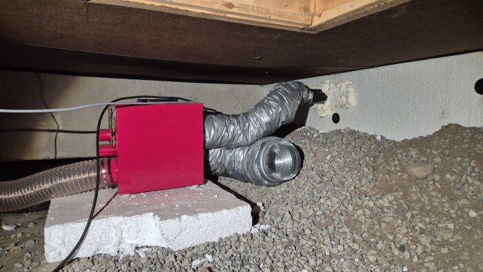 Krypgrundsavfuktare installerad med röranslutningar, placerad på frigolitblock ovanpå grus.