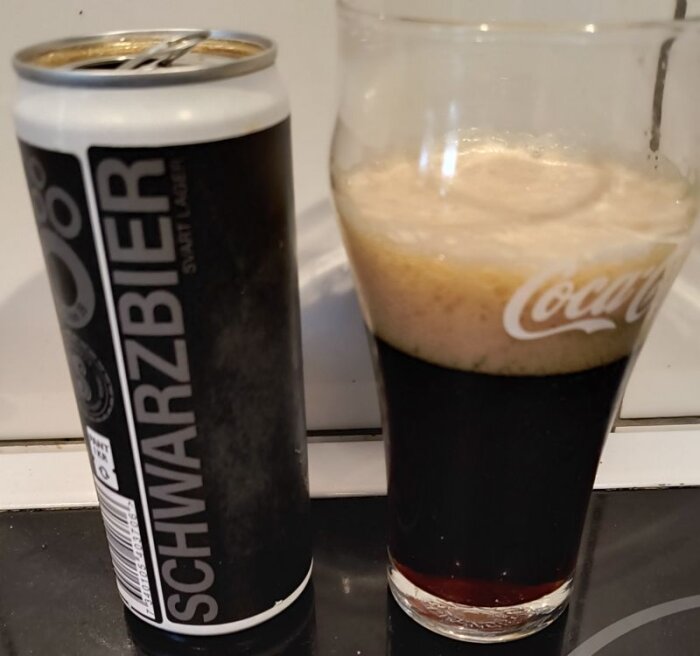En burk schwarzbier och ett glas med mörk öl och skum ovanpå, placerade på en bänkskiva.