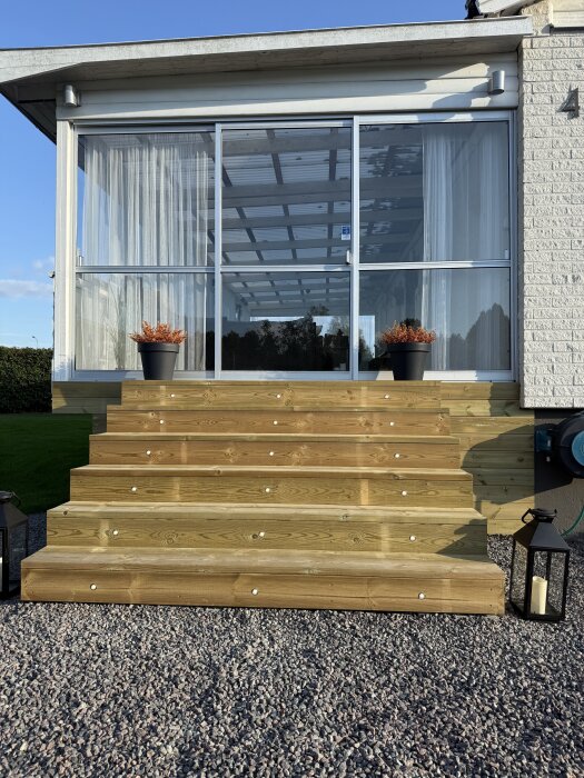 Trätrappa med 18 infällda decklights framför altan med glasväggar. Två svarta blomkrukor på sidorna och dekorativa ljuslyktor.