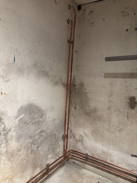 Kopparrör installerade i ett hörn av en oinredd källare, monterade längs väggen och golvet.