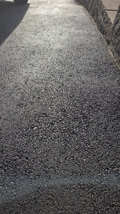 Nyasfalterad garageuppfart med varierande grovhet på asfalten, med partiklar synliga och ojämn yta.