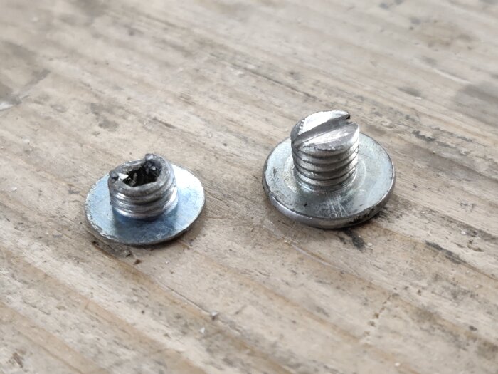 Två metallskruvar ligger på en träyta, en trasig och en hel med skårad topp.