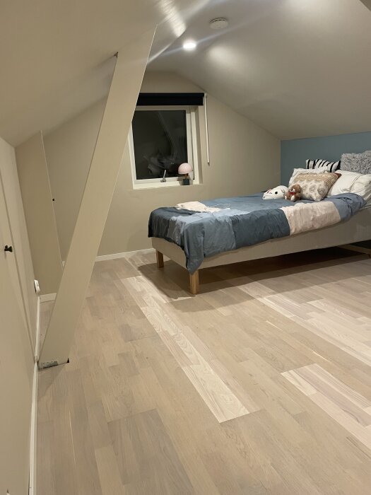Tonårsrum med ny parkett, synliga nyansskillnader. En säng med blågrå täcke, kuddar och mjukdjur är uppställd nära fönstret.