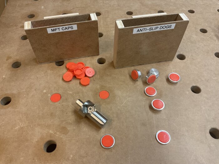 Förvaringslådor med texten "MFT CAPS" och "ANTI-SLIP DOGS" på en arbetsbänk, omgivna av orange tillbehör.