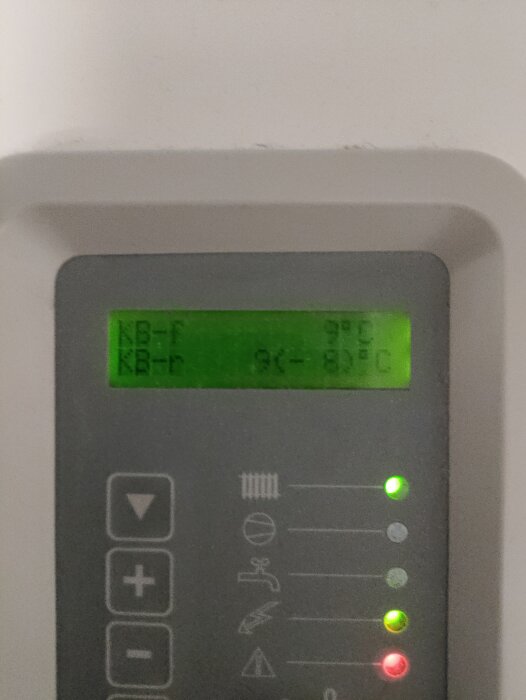 Digital display på värmepump visar temperaturer med gröna ljusindikatorer, ett rött ljus och knappar för justeringar.