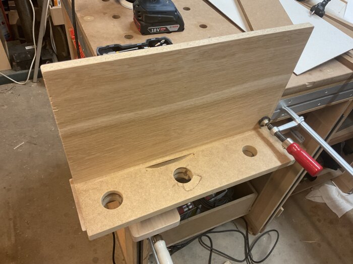 En enkel hylla med tre hål för förvaring av slipmaskiner, fastklämd på en arbetsbänk i verkstaden.