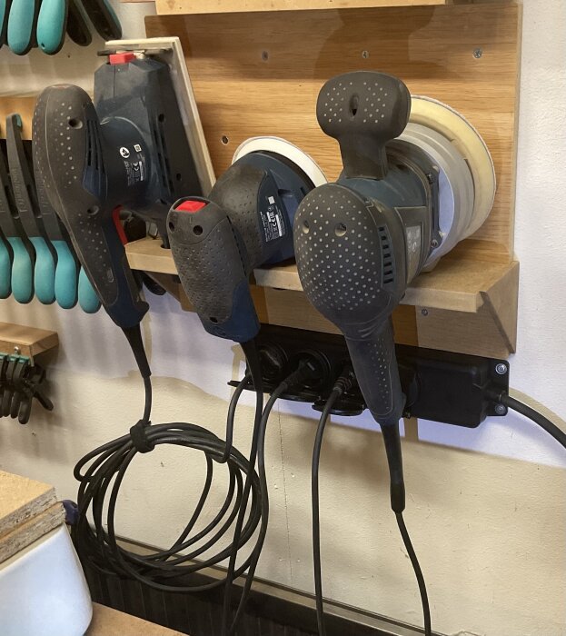 Slipmaskiner förvaras på vägghylla med grenuttag, nära arbetsbänken för enkel användning i verkstaden.