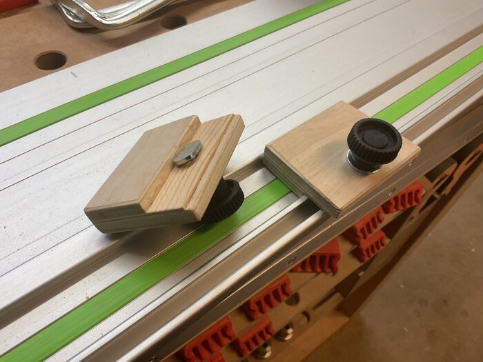 Två hemmagjorda kick back-stop av plywood med svarta justerbara knoppar, placerade på en arbetsyta i verkstaden.