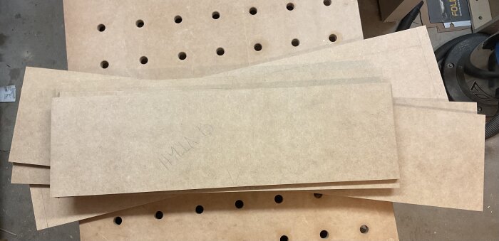 MDF-skivor märkta "HYLLA B" ligger på en arbetsyta med hål.