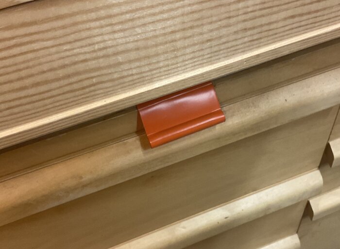 Trälåda med en röd tejpbit som handtag, använd för att dra ut en bricka med limdukar i en verkstadsmiljö.