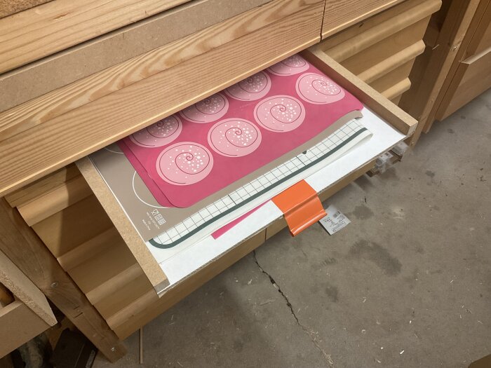 En låda med bakplåtsdukar i olika storlekar lagrade för att skydda arbetsbänken mot limspill i en verkstad.