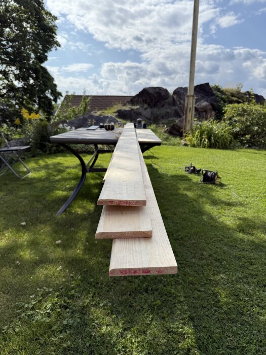 Träbrädor uppställda på ett utomhusbord, omgivna av grönska och himmel i bakgrunden.