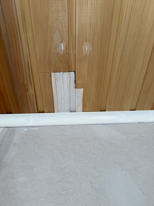 Träpanel med spikhål och en bit byggplyfa vid golvlister efter renovering av ett rum.