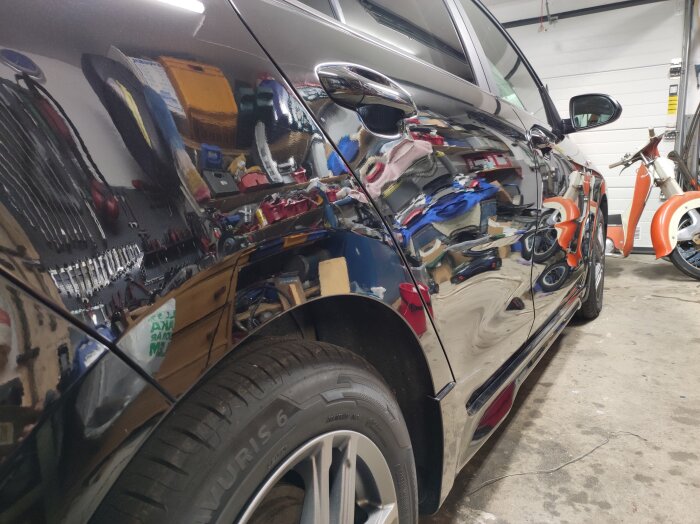 Höger sida av en polerad bil i ett garage med reflektioner av verktyg och en motorcykel på karossen.