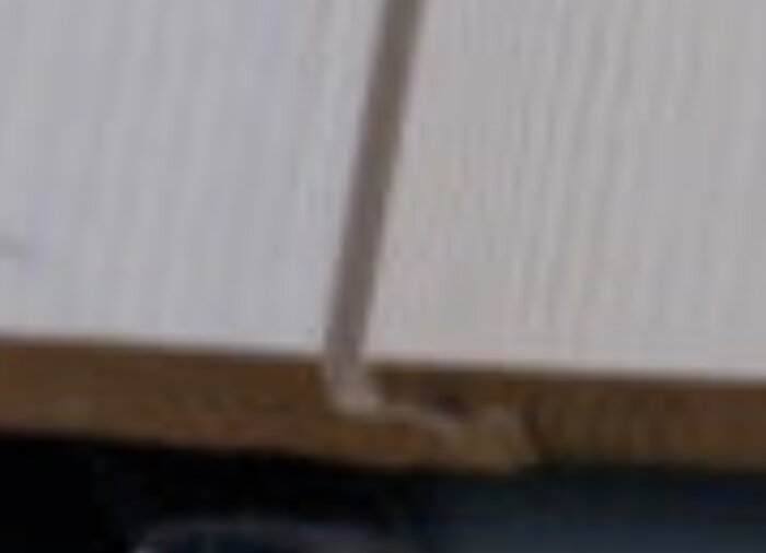 Närbild av vitmålad spontad träpanel med fokus på skarv och kant.