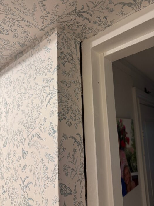 Skarv mellan blommig tapet och vit dörrkarm med en synlig glipa.