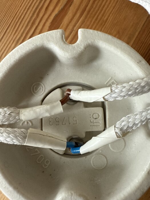 Lamphållare med två vita textilklädda kablar, en med blå ledare och en med brun ledare, anslutna med tejp på en träyta.