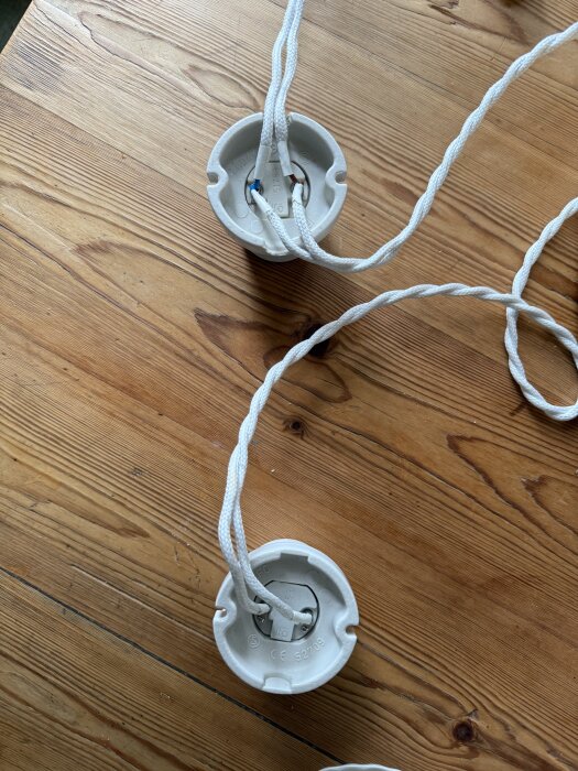 Två vita lamphållare med tvinnade sladdar ligger på ett träbord, kopplade i serie.