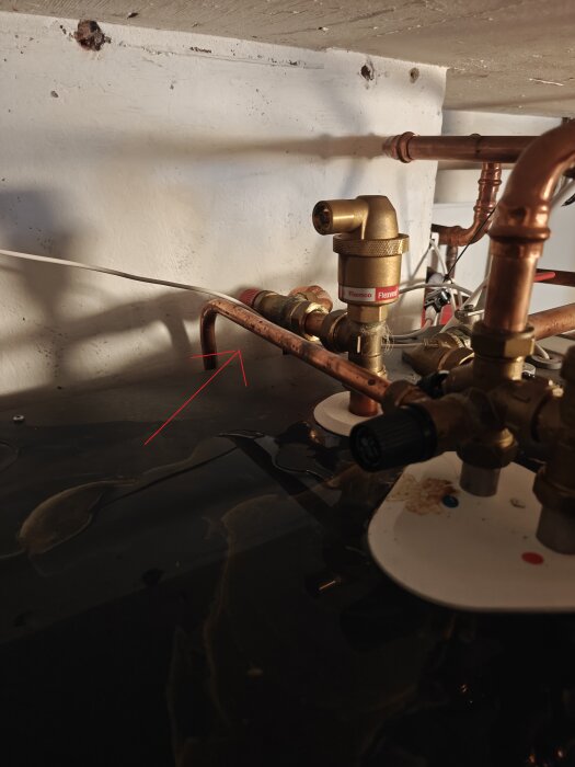 Ventil och kopparrör med röd pil visar vattenansamling ovanpå en pump.