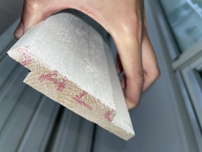 Närbild på ändträet av en mellangrå struken ytterpanel, hållen i en hand, med märken på träytan.