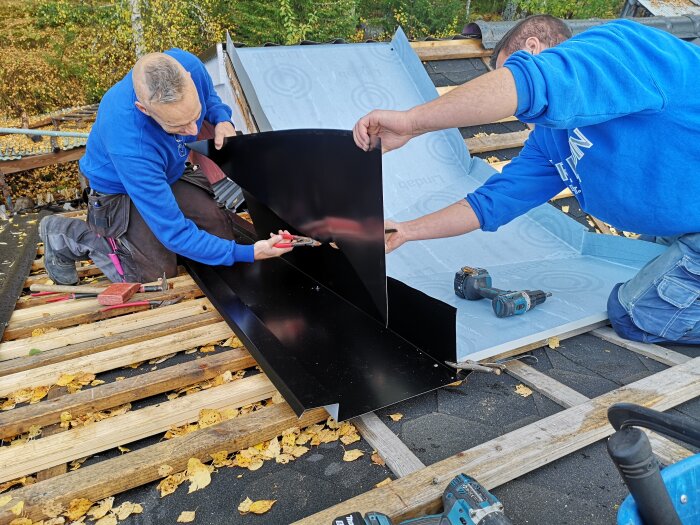 Plåtslagare installerar svart plåt på tak, omgivna av verktyg och löv.