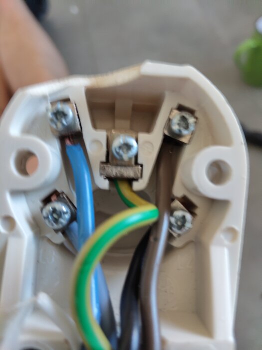 Elanslutningsplint med kablar i olika färger, inklusive blå, gul/grön och brun, anslutna med skruvar.