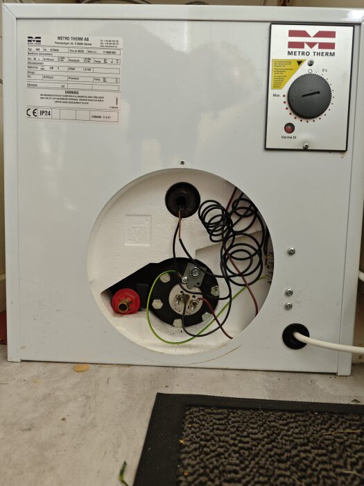Varmvattenberedare från Metro Therm med öppen panel visar inre kablar och komponenter på golvet. Skala och märkningar synliga.