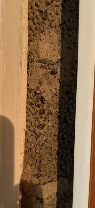 Närbild av en murvägg i en källare, med textur som liknar blåbetong, omgiven av ljust målat trä och skuggor.