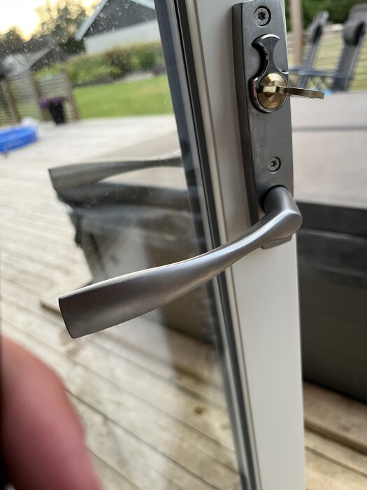 Fönsterhandtag i metall på glasdörr med altandäck synligt utanför.