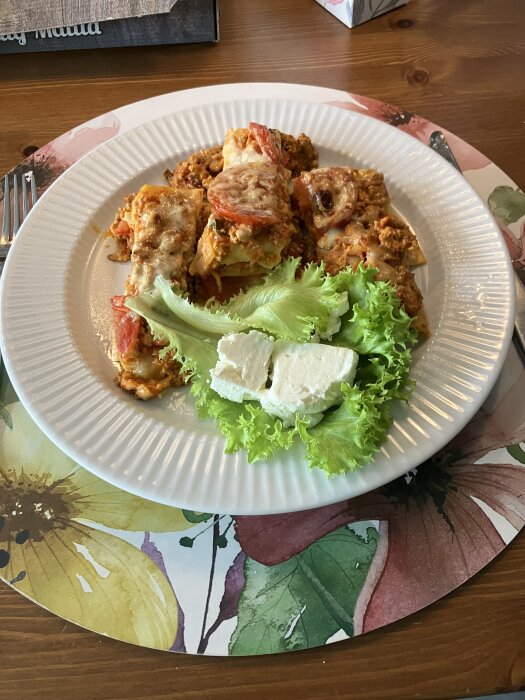 Lasagne utan bechamelsås serverad med sallad och skivor av halloumi på en vit tallrik med en blommig underlägg.