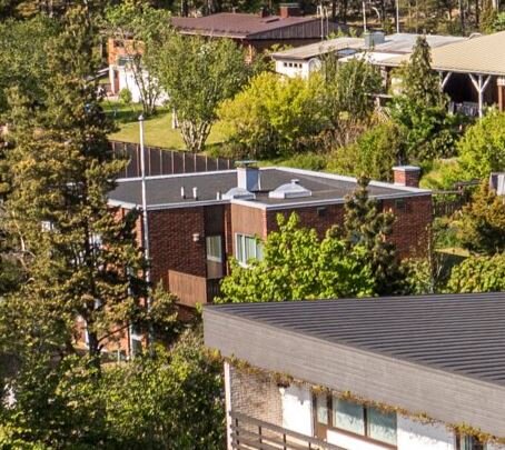 Tak med två takfönster omgivet av grönska, hus syns i bakgrunden.