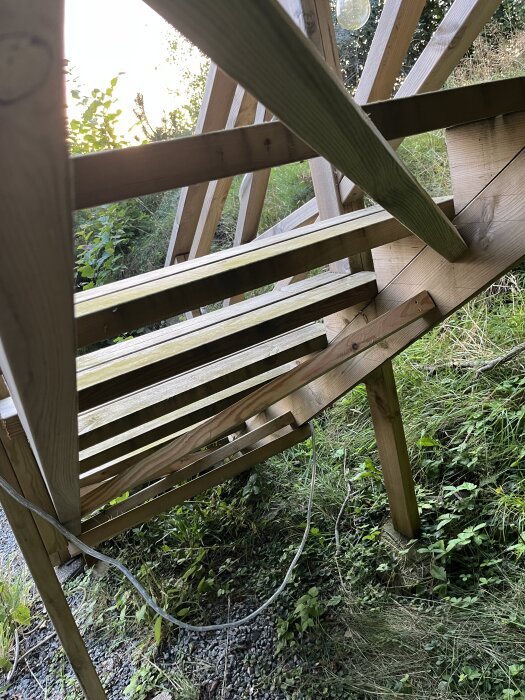 Trätrappa utomhus, nyligen förstärkt för ökad stabilitet, med omgivande grönska och en genomgående kabel.