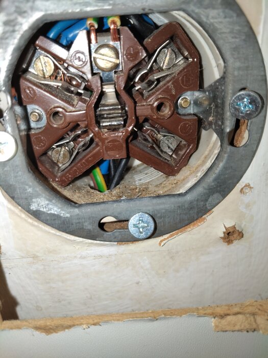 Närbild av en gammal och sliten elkontakt med exponerade kablar i väggen, del av ett byte av trasig spishäll i ett nyinköpt hus.