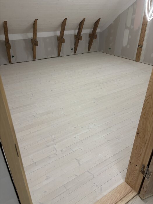 Ljust trägolv i rum med träbalkar och obehandlade väggar, efter behandling med lut och innan applicering av olja.