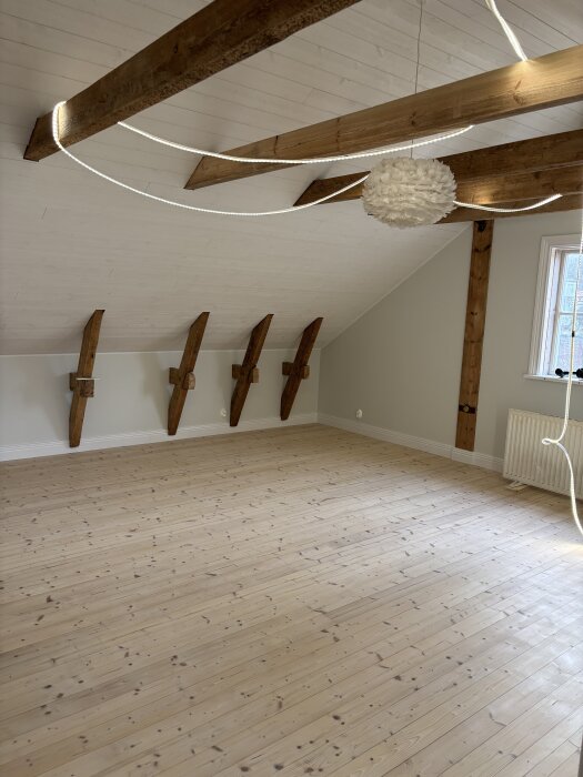 Ljusa trägolv i ett rum med synliga träbjälkar i taket och en modern ljuskälla hängande, efter behandling med lut och naturell olja.