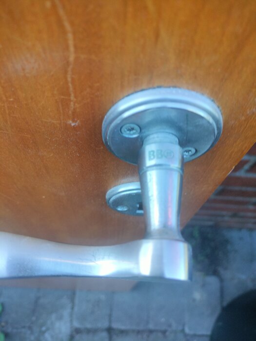 Dörrhandtag av metall monterat på en träfärgad dörr, sedd utifrån.