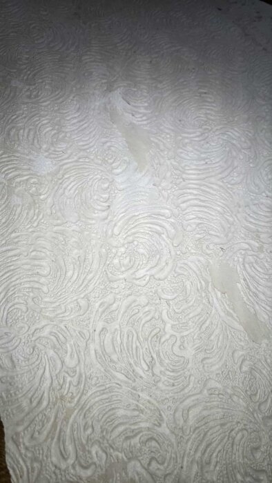 Närbild av en vägg med ljus, strukturerad tapet, där små mögelfläckar syns i fördjupningarna.